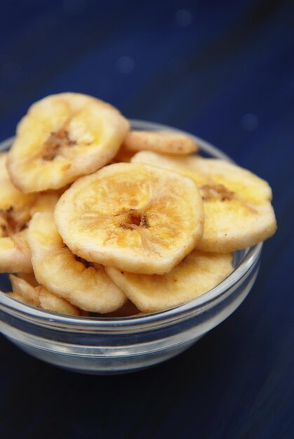 Gezonde snack gemaakt van bananenchips. Gesneden Banaanstukken in Glaskom op Donkerblauwe Achtergrond. Verticale afbeelding.