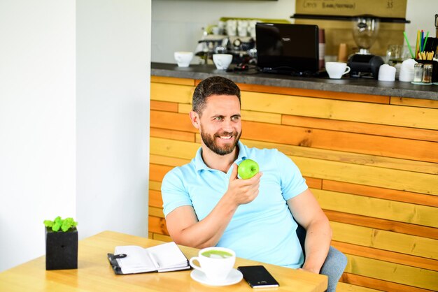 Gezonde snack. Lunch eet appel. Gezonde gewoonten. Koffiepauze om te ontspannen. Gezonde man zorg vitamine voeding tijdens de werkdag. Fysiek en mentaal welzijnsconcept. De mens zit eet groen appelfruit.