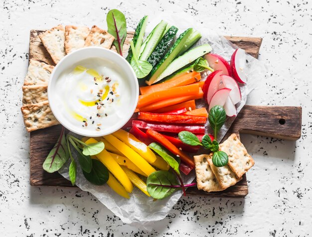 Gezonde snack rauwe groenten en yoghurtsaus op een houten snijplank op een lichte achtergrond