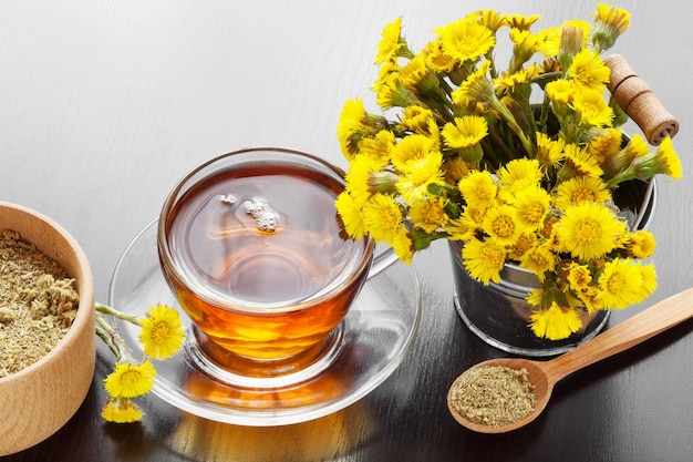 Gezonde thee in de close-upemmer van de glaskop met klein hoefbladbloemen en mortier