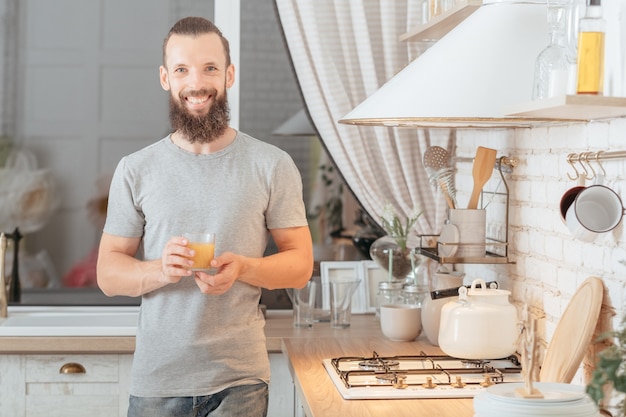 Gezonde veganistische levensstijl. Evenwichtige voeding. Man in de keuken met een glas jus d'orange, glimlachend. Venstermuur vervagen.