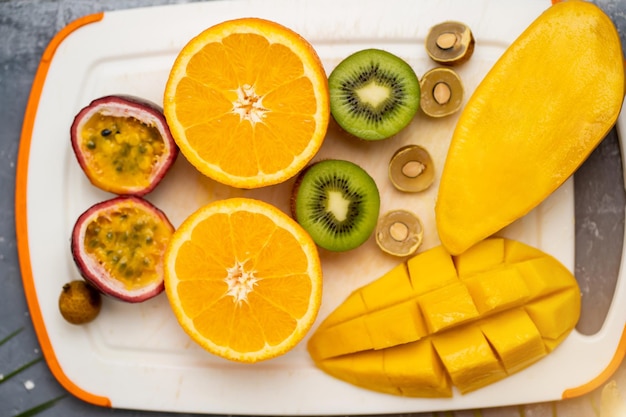 Gezonde veganistische snack van rauw tropisch exotisch fruit. Close-up van gesneden verse mango, sinaasappel, kiwi, passievrucht, longan op witte snijplank. Bovenaanzicht, plat gelegd.