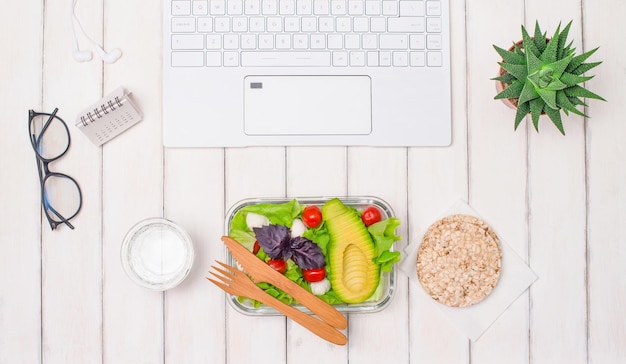 Gezonde veganistische zelfgemaakte lunch in lunchbox op witte tafel met laptop koptelefoon kalender brillen