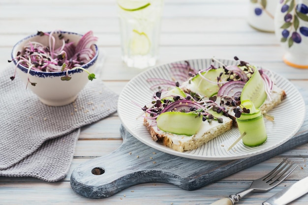 Gezonde vegetarische bruschetta's met brood micro greens kaaskomkommers en rode ui op lichte rustieke houten tafel