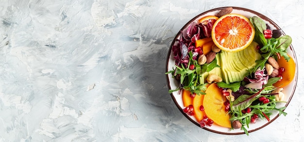 Gezonde vegetarische buddha bowl salade met avocado persimmon bloedsinaasappel noten spinazie rucola en granaatappel op een lichte achtergrond Lang banner formaat bovenaanzicht