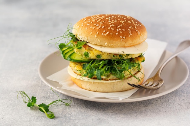 Gezonde vegetarische burger met ei en erwtenscheuten en zaden microgroen, frisse salade, komkommerschijfje op een houten snijplank op lichte achtergrond. Selectieve focus