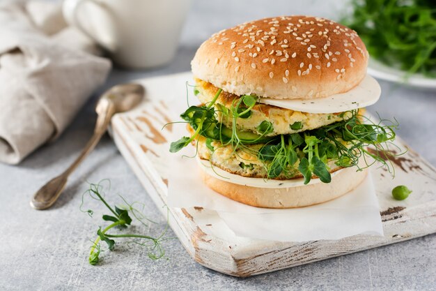 Gezonde vegetarische hamburger met ei en erwten scheuten en microgroene zaden, verse salade, komkommer segment op een snijplank houten op lichte achtergrond. Selectieve aandacht.