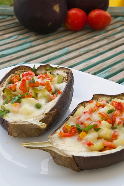 Gezonde vegetarische lunch: ovengebakken gevulde aubergines met groenten en kaas op een wit bord. Groente op de achtergrond.