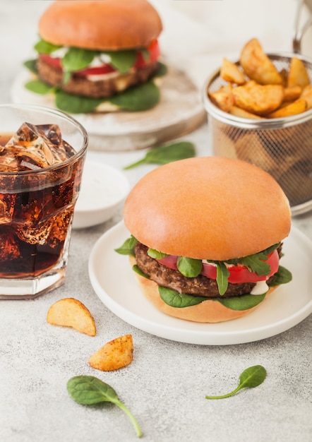 Gezonde vegetarische vleesvrije hamburgers op ronde keramische plaat met groenten op lichte tafel met aardappelpartjes en glas cola.