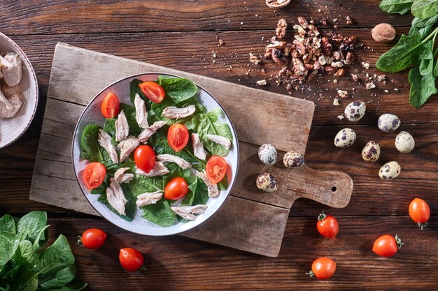 Gezonde vers bereide salade van kwarteleitjes, vlees, tomaten en spinazie in een plaat op een houten bord op de keukentafel. Dieet lunch. Plat leggen