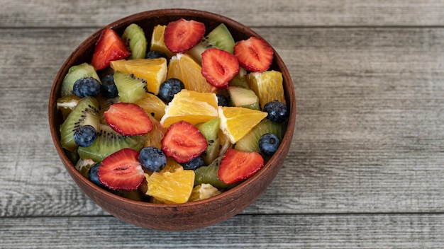 Foto gezonde verse fruitsalade in bruine kom op grijze achtergrond bovenaanzicht