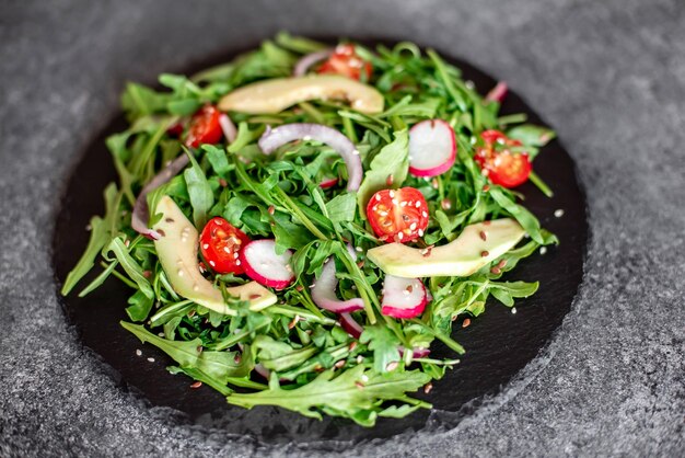 Gezonde verse groentesalade tomaten rucola avocado radijs op een stenen achtergrond