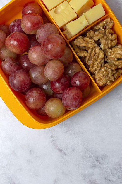 Gezonde voeding in plastic bakjes klaar om te eten met kaas, druiven en walnoten op de werktafel. Om mee te nemen. Walnoten