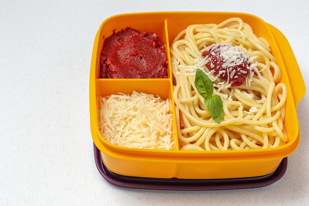 Gezonde voeding in plastic bakjes klaar om te eten met zelfgemaakte spaghetti met tomaat, kaas en basilicum op de werktafel. Italiaans eten. Wegnemen.