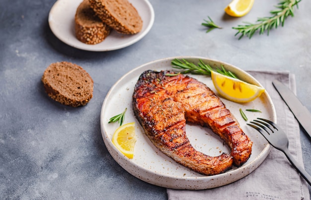 Gezonde voeding omega-concept. gegrilde zalm steak met citroen, rozemarijn geserveerd op een witte plaat op grijze steen