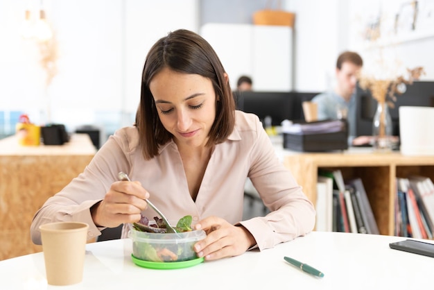 Gezonde voeding op de werkplek concept. Vrij Spaanse vrouw die een salade eet in het kantoor.