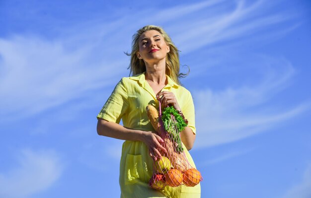 Gezonde voeding tas met boodschappen Herbruikbare eco tas om te winkelen Vrouw met string boodschappentas met fruit en brood op hemelachtergrond Zero waste concept meisje in jurk met string tas shopper