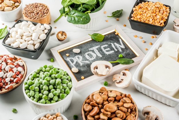 Gezonde voeding veganistisch voedsel, plantaardige eiwitbronnen: tofu, veganistische melk, bonen, linzen, noten, sojamelk, spinazie en zaden. Bovenaanzicht op witte tafel.