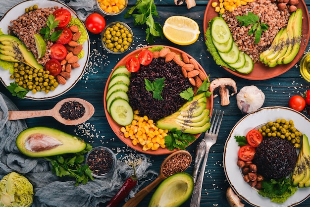 Gezonde voeding zwarte rijst boekweit avocado cherry tomaten groene erwten en hazelnoot op een houten achtergrond bovenaanzicht vrije ruimte voor uw tekst