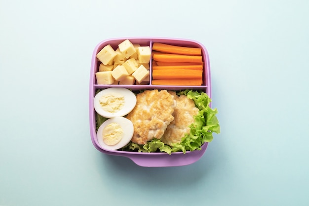 Gezonde voedsel plastic lunchcontainer met inbegrip van kippenkoteletten, kippenei, salade, wortelwiggen, kaasplakken.