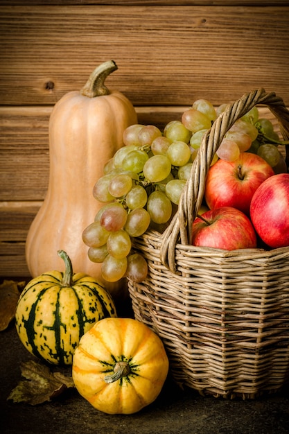 Gezonde voedselinhoud, stilleven van pompoenpompoen, minipompoenen, rieten mand met groene en gele druiven, rode appels, op een donkere tafel, houten achtergrond