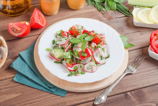 Gezonde voedselsalade van verse groenten, radijs, komkommers in een witte plaat op een donkere houten achtergrond