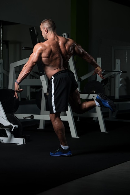 Gezonde volwassen man staat sterk in de sportschool en buigt spieren Gespierde atletische bodybuilder Fitness man poseren na oefeningen