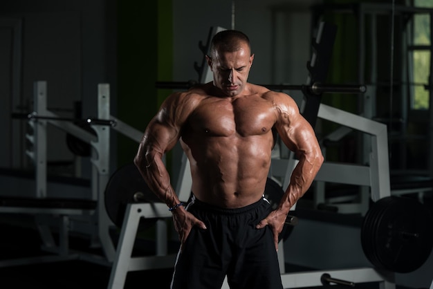 Gezonde volwassen man staat sterk in de sportschool en buigt spieren Gespierde atletische bodybuilder Fitness man poseren na oefeningen