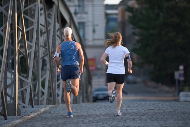 gezonde volwassen paar joggen in de stad in de vroege ochtend met zonsopgang op de achtergrond