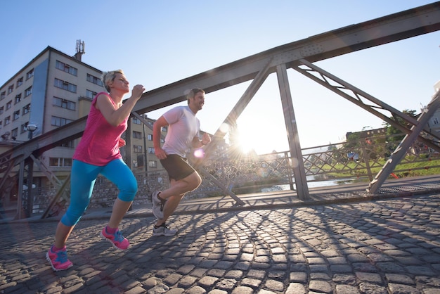 gezonde volwassen paar joggen in de stad in de vroege ochtend met zonsopgang op de achtergrond