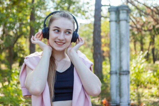 Gezonde, vrolijke fitte vrouw die naar muziek luistert in stereokoptelefoons in het park