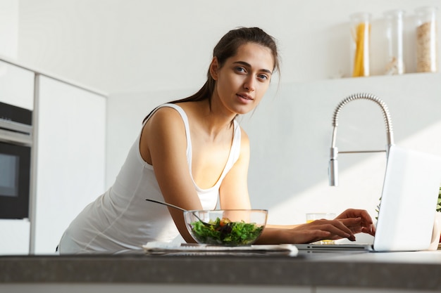 Gezonde vrouw in de keuken die dagelijkse ochtendroutine bevindt zich dichtbij salade.