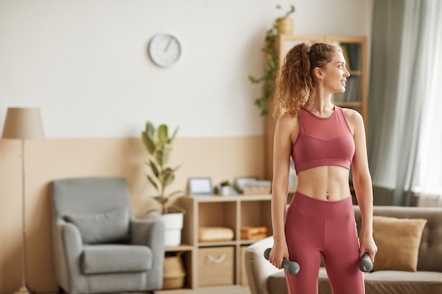 Gezonde vrouw in sportkleding trainen met halters in de kamer thuis