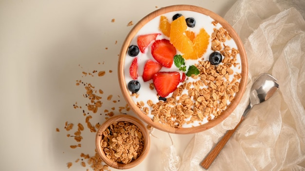 Gezonde yoghurtkom met verse aardbeien, bosbessen, sinaasappelen en muesli op witte tafel. vlak