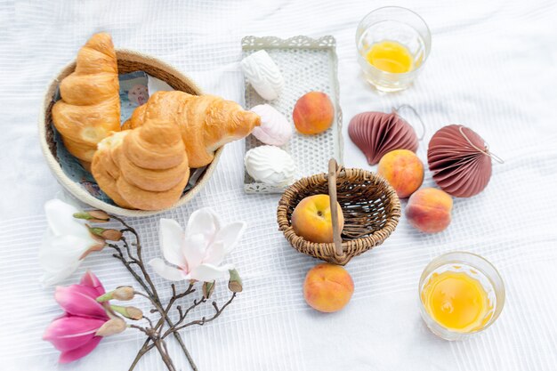 Gezonde zomerpicknick aangelegd op witte doek op groen gras met croissants, vers fruit, sap en marshmallows.