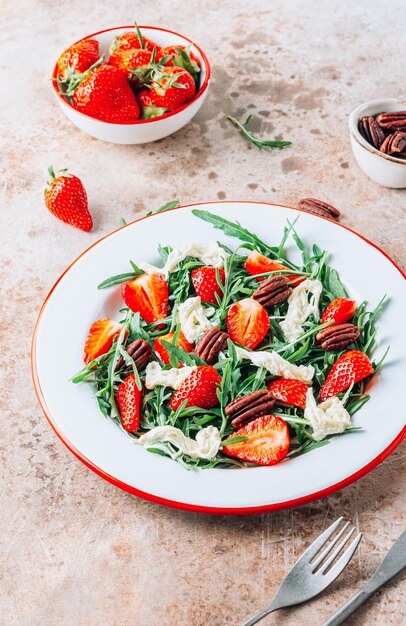 Gezonde zomersalade met aardbei rucola stracciatella en pecannoten op beige rustieke achtergrond