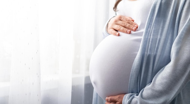 Gezonde zwangerschap zijaanzicht zwangere vrouw met dikke buik vergevorderde zwangerschap in handen banner copyspace voor tekst elegante moeder wachtende baby