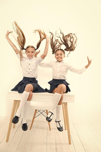 Gezonder haar van wortel tot punt schattige kleine meisjes met rondvliegend haar zittend op het bureau schattige kleine kinderen met langharige paardenstaarten die schooluniform dragen luxe haarextensies