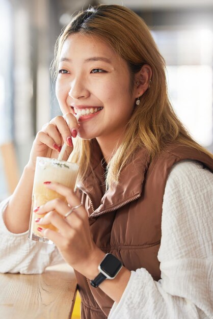 Gezondheid Aziatische vrouw en smoothie voor dieet in een café en geluk voor welzijn en denken Japan vrouwelijk en gelukkig meisje met milkshake ontspannen pauze en vrolijk dagdromen bij een restaurantraam