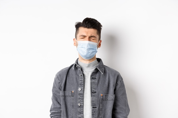 Gezondheid, covid en pandemie concept. Triest huilende man in medisch masker boos over quarantaine, staande op een witte achtergrond.