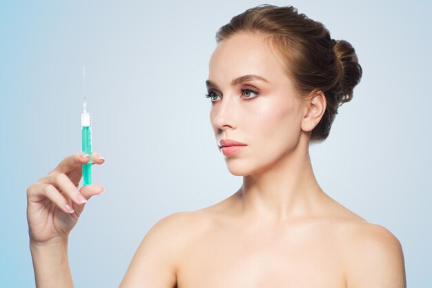gezondheid, mensen, cosmetologie, plastische chirurgie en schoonheidsconcept - mooie jonge vrouw met spuit met injectie over blauwe achtergrond