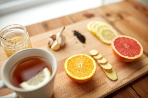 gezondheid, traditionele geneeskunde, folk remedie en etnoscience concept - kopje gemberthee met honing, citrus en knoflook op houten ondergrond