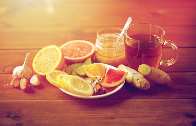 gezondheid, traditionele geneeskunde, volksremedies en etnoscience concept - kopje gember thee met honing, citrus en knoflook op houten achtergrond