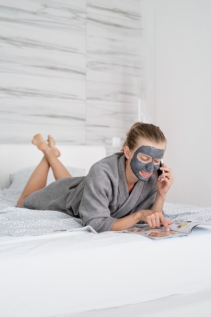 Gezondheid van vrouwen. Spa en wellness. Vrouw met gezichtsmasker ontspannen liggend op het bed een tijdschrift lezen