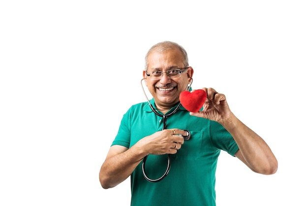 Gezondheidsbewuste Indiase Aziatische senior mannelijke volwassene die de hartslag controleert met een stethoscoop, speelgoedhart of appel in de andere hand houdt en een goed teken toont