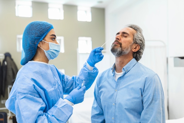 Gezondheidswerker met beschermende uitrusting voert coronavirus-uitstrijkje uit op oudere man. neusuitstrijkje voor covid19.