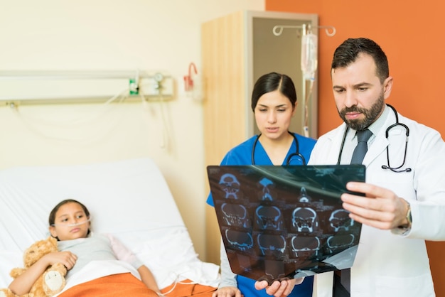 Gezondheidswerkers kijken naar röntgenfoto's terwijl ze discussiëren tegen de patiënt die op bed in het ziekenhuis ligt