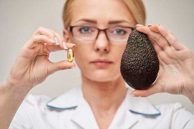 Gezondheidszorg en dieetconcept - arts-voedingsdeskundige of cardioloog die visolie in capsules voor vitamine D en omega-3-vetzuren en avocado houdt
