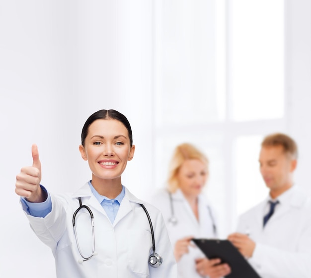 gezondheidszorg en geneeskundeconcept - glimlachende vrouwelijke arts met stethoscoop die duimen toont