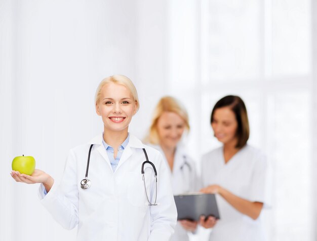 gezondheidszorg en geneeskundeconcept - glimlachende vrouwelijke arts met stethoscoop en groene appel